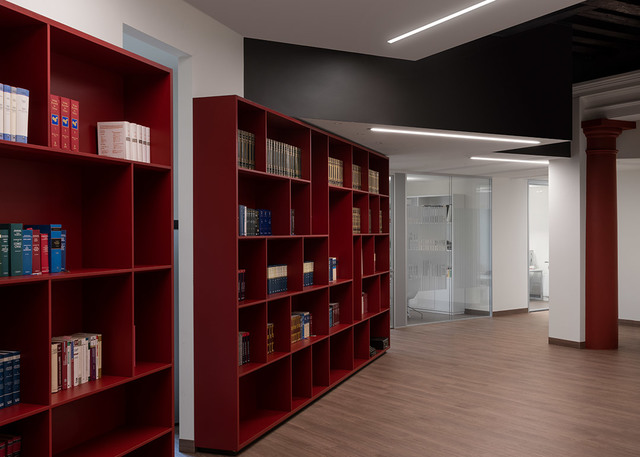 Office library with red shelving units and books, illuminated by Artemide linear LED ceiling lights on a dark ceiling.