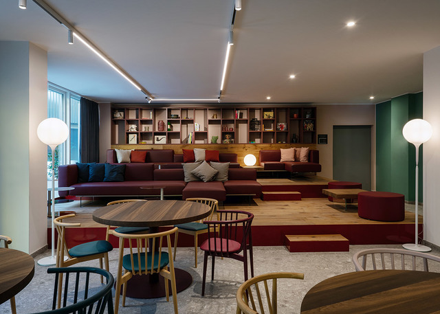 Modern lounge with Artemide floor lamps featuring white globe shades, track lighting on ceiling, burgundy sofas, and colorful dining chairs