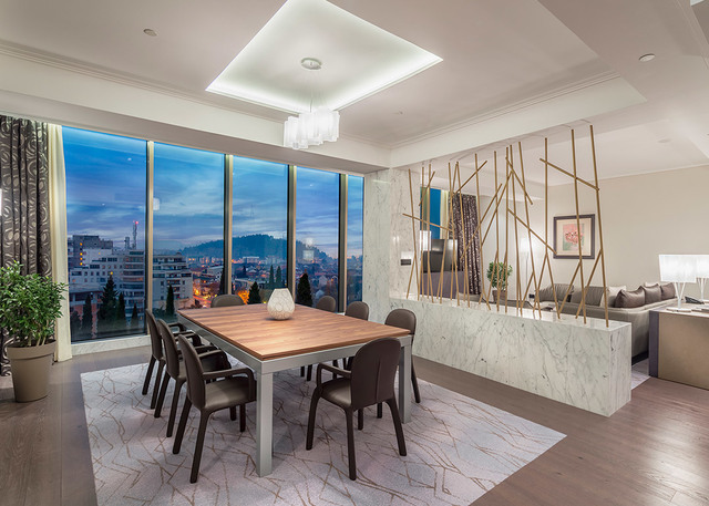 Elegant dining room with a chandelier over a wooden table, floor-to-ceiling windows, marble partition, and golden decorative rods