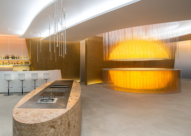 Modern bar interior with pendant lights on thin cables, curved golden bar counter with fringe curtain, and warm ambient lighting