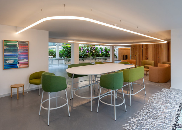 Modern office lounge with a curved Artemide LED ceiling light strip over a white oval table with green bar stools