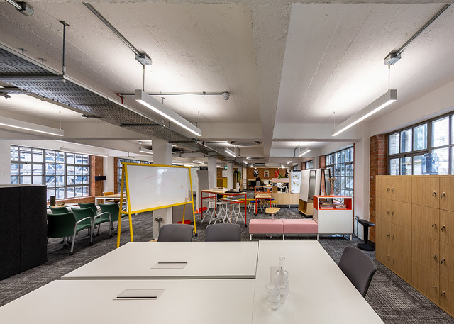 Open-plan office with linear pendant LED lights illuminating workstations, collaborative seating areas, and whiteboards in a modern workspace