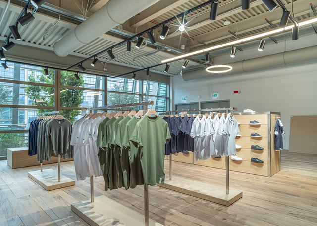 Retail clothing store interior with Artemide track spotlights and circular pendant lights illuminating garment racks and wooden displays.