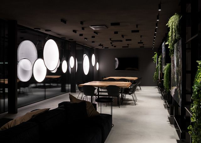 Dark modern lounge with Artemide large circular glowing pendant lights, live green wall, wooden tables, and ceiling track spotlights