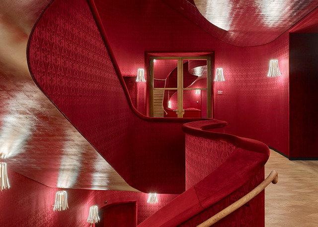 Dramatic red staircase with curved walls and ceiling, accented by wall-mounted fringe pendant lamps casting warm light.