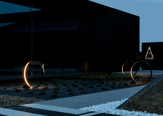 Two circular Artemide outdoor floor lamps with warm LED arc lighting, installed in a dark landscaped entrance area at dusk.