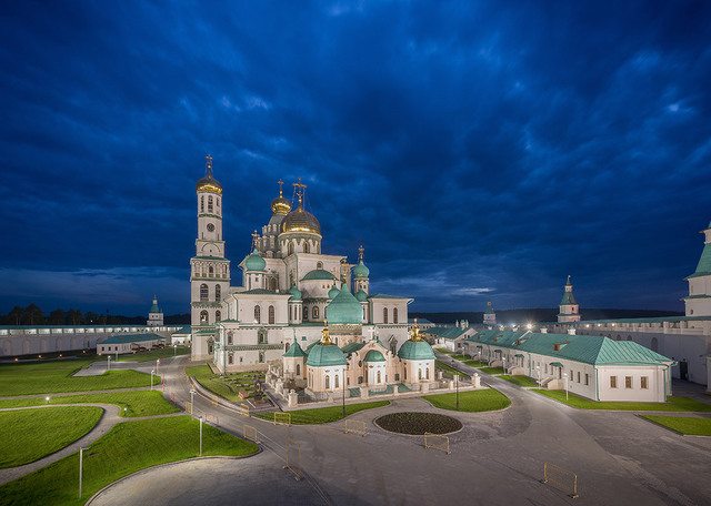 New Jerusalem Monastery illuminated at dusk, featuring white facades, turquoise domes with golden crosses, and warm outdoor lighting.