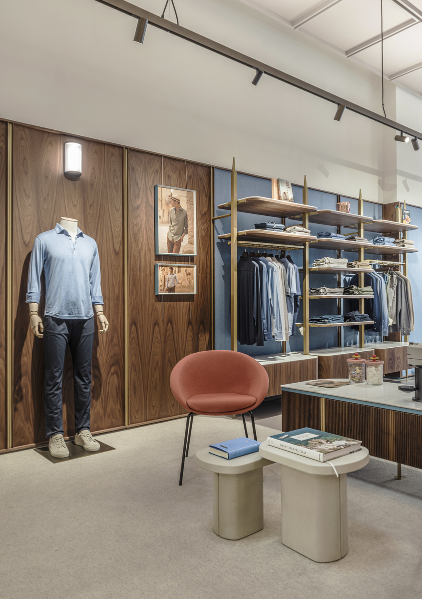 Boutique interior with Artemide wall sconce illuminating wood-paneled wall, mannequin, open wardrobe, pink chair, and display table.
