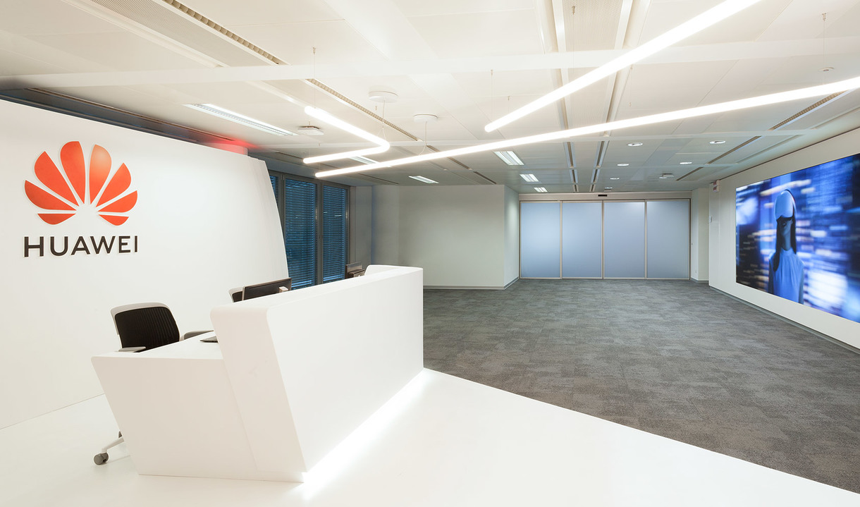Huawei office reception with white desk, Artemide linear LED ceiling lights illuminating a modern open workspace with carpet flooring.