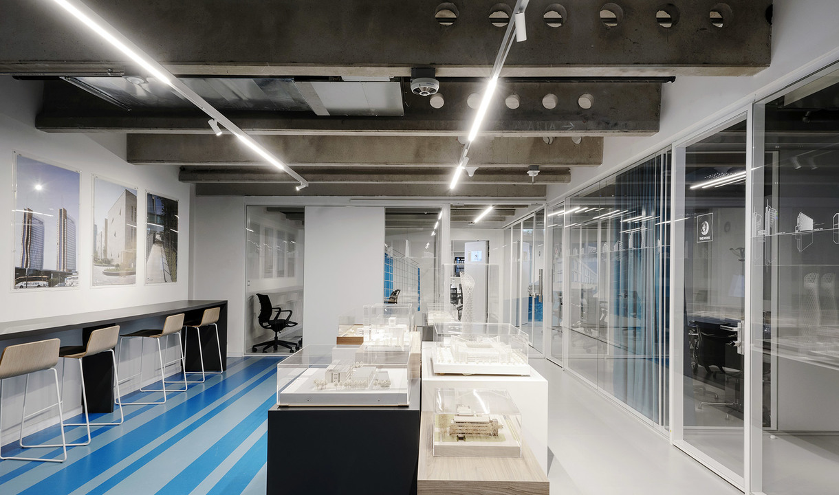 Modern office with Artemide linear LED ceiling lights illuminating architectural models on display tables and glass-partitioned workspaces.