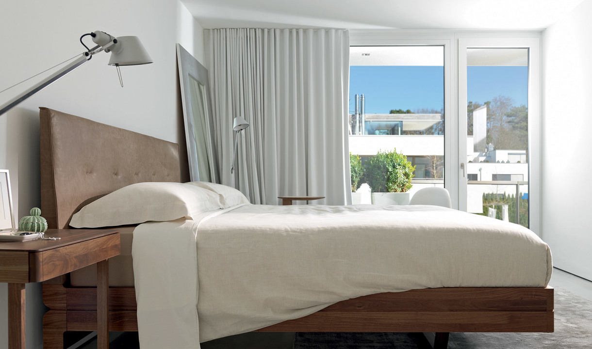 Modern bedroom with Artemide Tolomeo floor lamp in silver beside a wooden bed with neutral bedding, large windows with white curtains