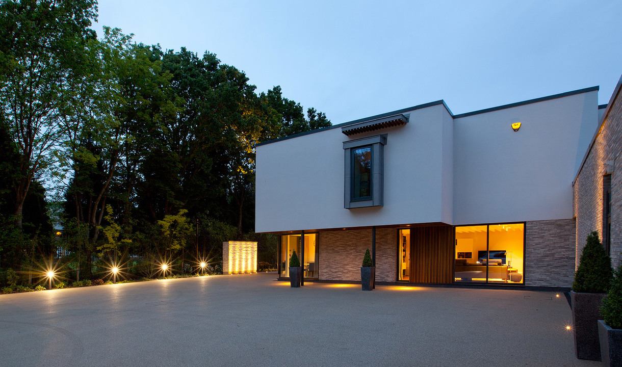 Modern villa exterior at dusk with warm Artemide ground and wall lights illuminating the driveway, entrance, and façade.