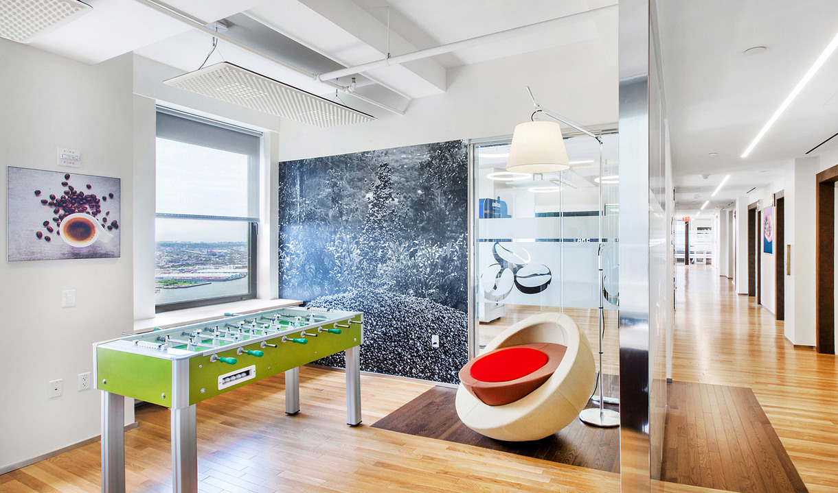 Modern office lounge with foosball table, pod chair, and Artemide Tolomeo Mega floor lamp near glass partition wall