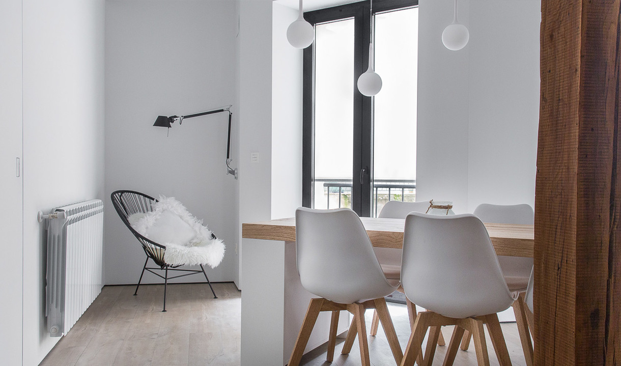 Minimalist dining area with white tulip chairs, wood table, two white globe pendant lights, and a reading lamp near a lounge chair.