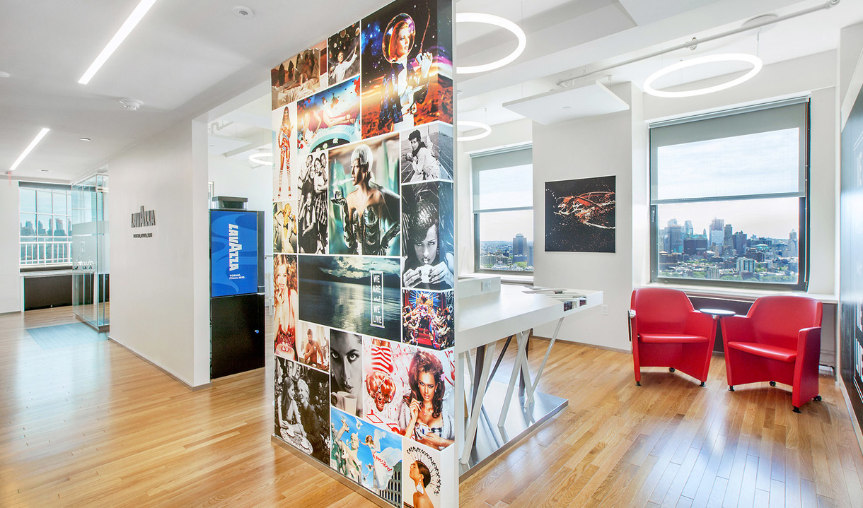 Modern office with Artemide circular pendant lights, collage-covered column, hardwood floors, red chairs, and city skyline view.