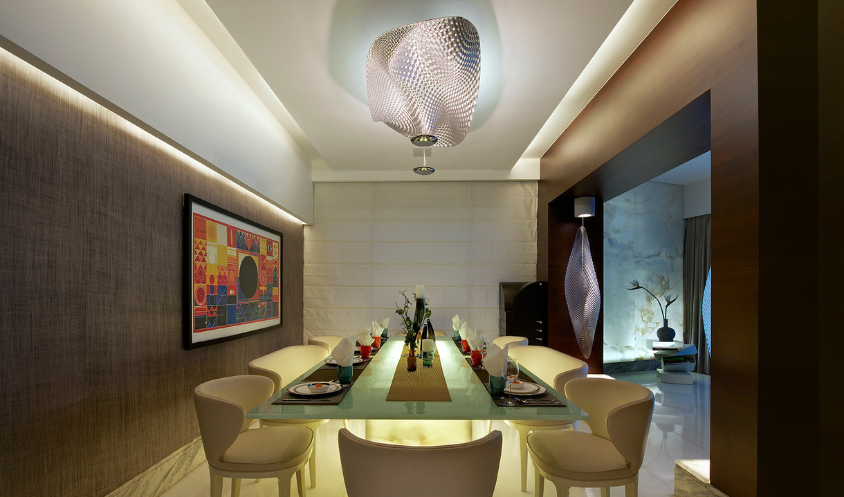 Elegant dining room with a large sculptural ceiling lamp featuring a woven metallic shade, illuminating a glass dining table with cream chairs.