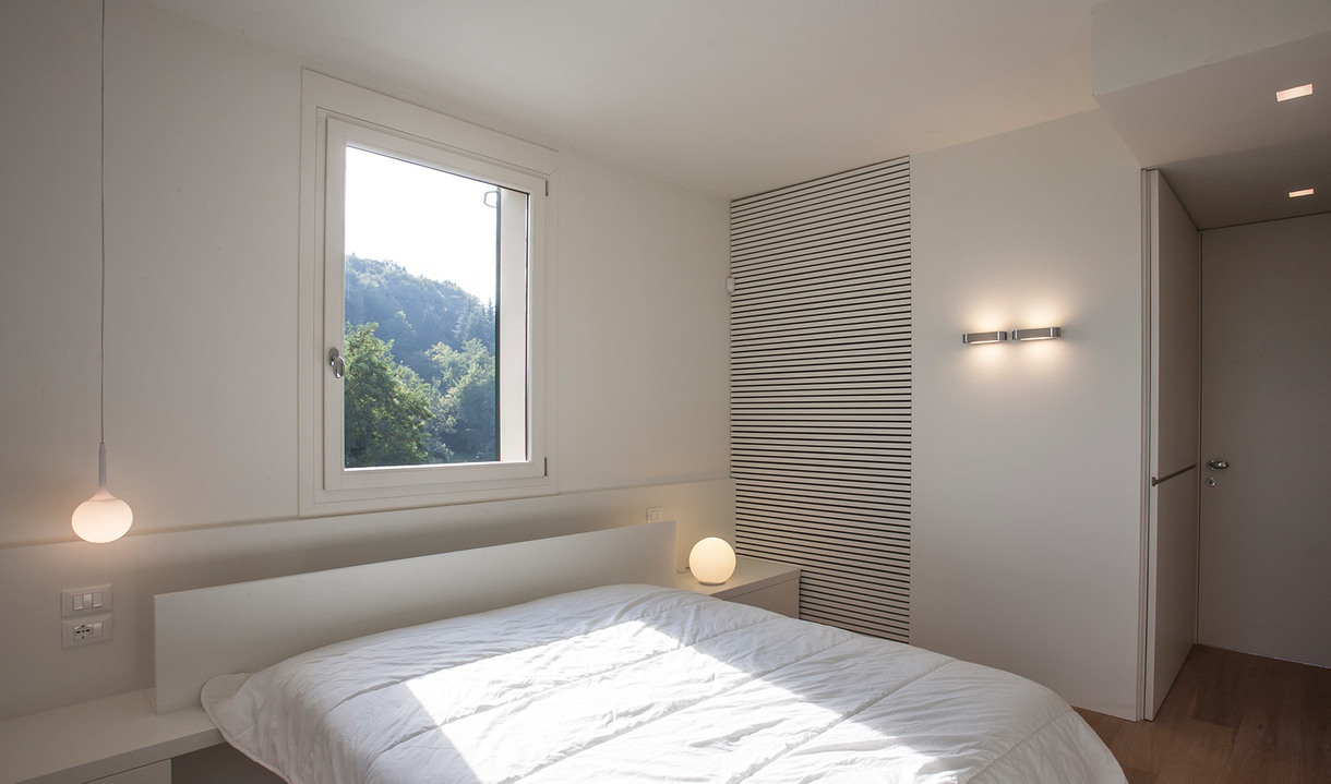 Minimalist white bedroom with two spherical pendant lamps, a bedside globe lamp, and a horizontal wall light near the door.