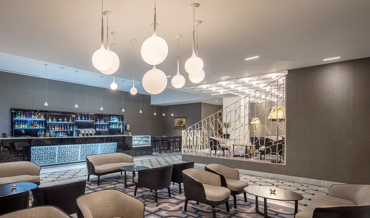 Elegant hotel lounge with Artemide globe pendant lights in varying sizes, illuminating seating area, bar counter, and decorative staircase.