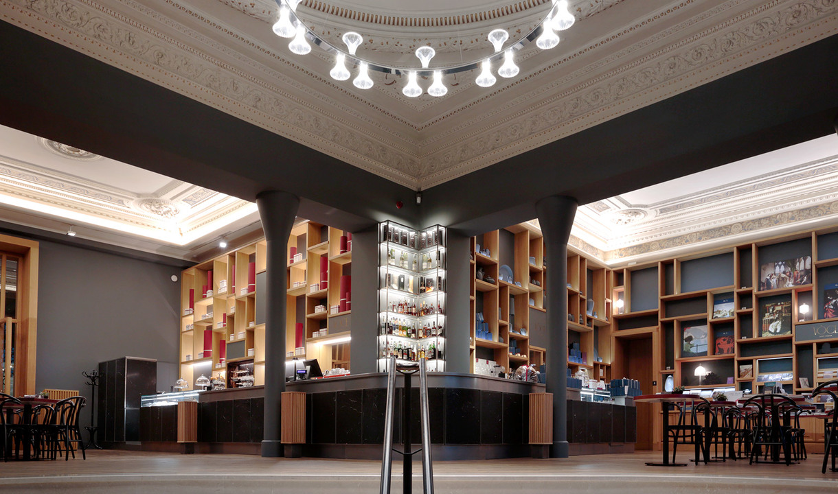 Elegant bar interior with ornate ceiling, wall shelving, and a central floor lamp with multiple white globe shades providing ambient lighting