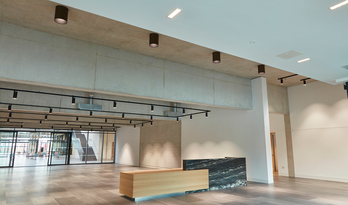 Modern lobby with cylindrical ceiling spotlights, black track lights on mezzanine rail, and a two-tone reception desk on wood floor
