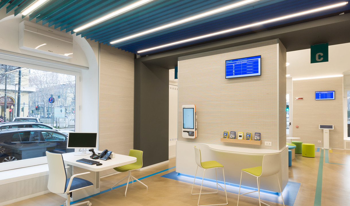 Modern bank interior with Artemide linear LED ceiling lights illuminating a bright service area with workstations and digital displays