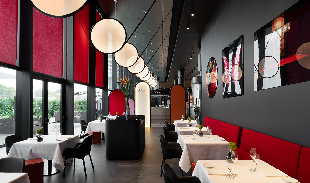 Elegant restaurant interior with a row of large spherical white pendant lamps illuminating red-accented dining area with dark walls.
