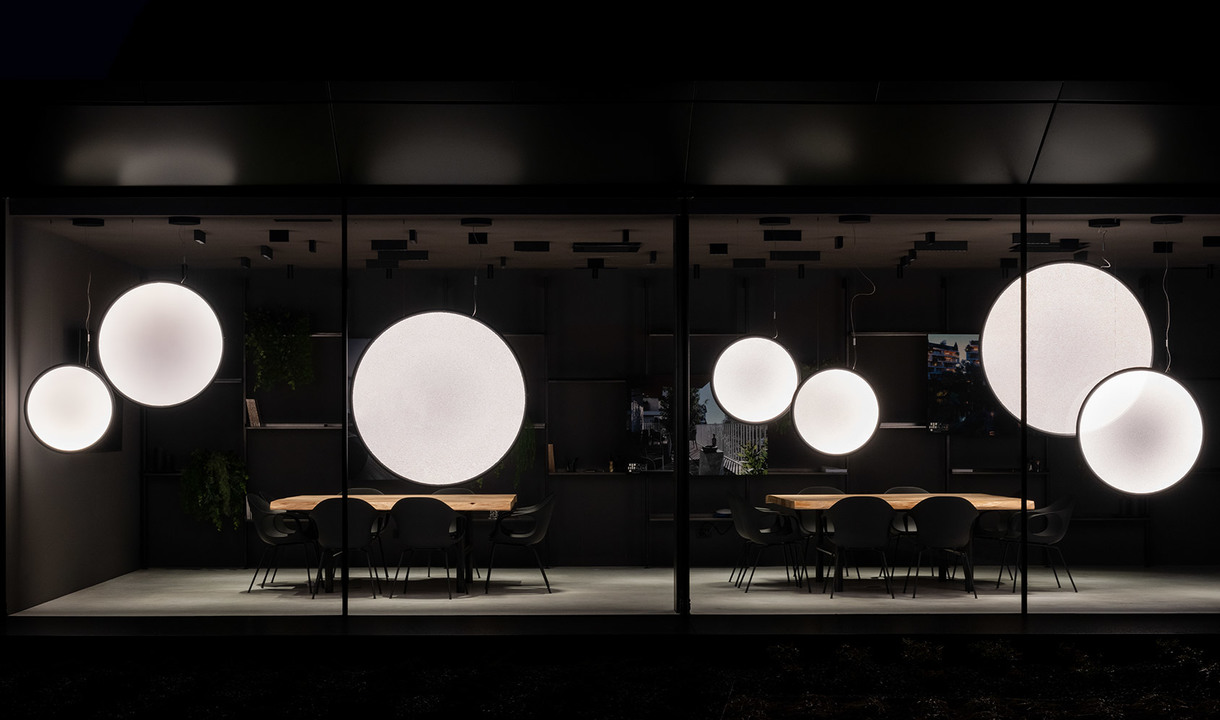 Artemide showroom at night: multiple glowing white spherical pendant lamps of varying sizes suspended over a dark dining area