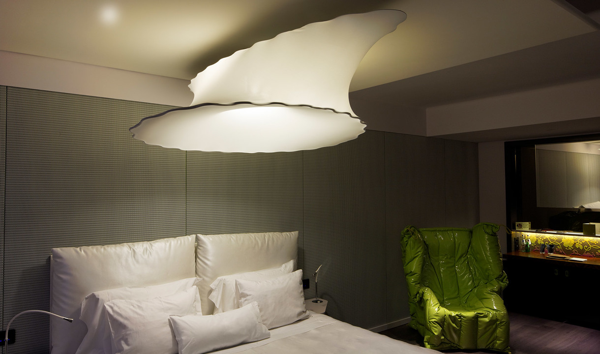 Artemide large cloud-shaped pendant lamp illuminating a modern bedroom with white bedding and a green armchair.