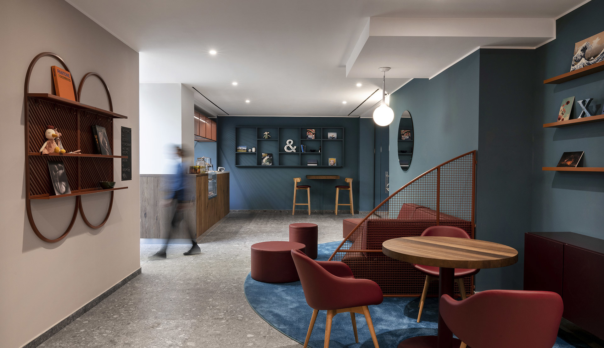Modern lounge with blue walls, red chairs, round tables, globe pendant light, recessed spotlights, and circular wall shelves.