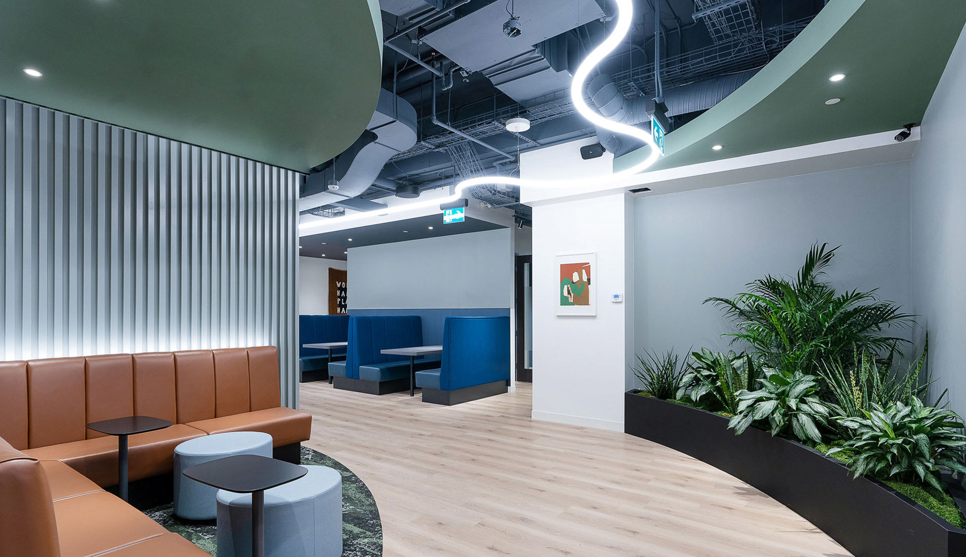 Modern office lounge with sinuous LED ceiling light, recessed spotlights, leather seating, blue booths, and indoor plants.