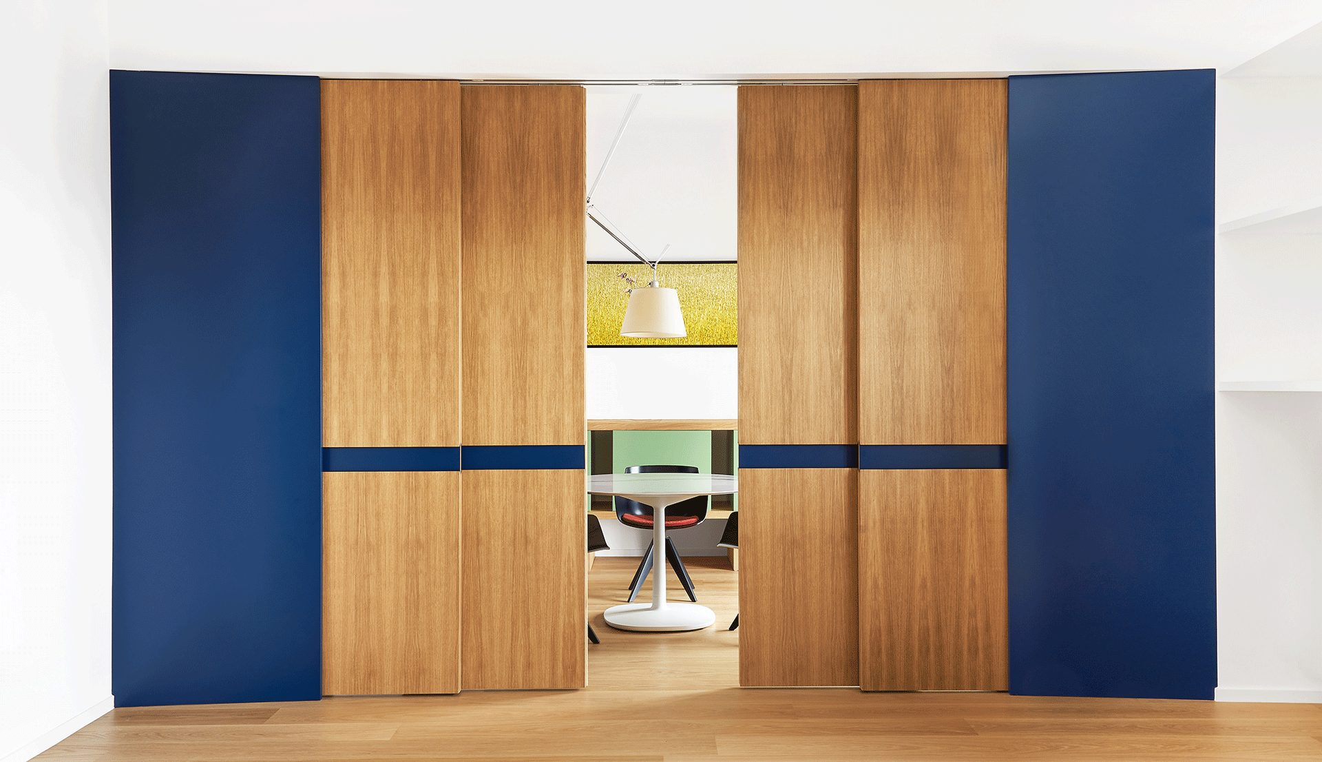 Artemide Tolomeo pendant lamp illuminates a modern dining area with round table, visible through sliding wood and blue panels.