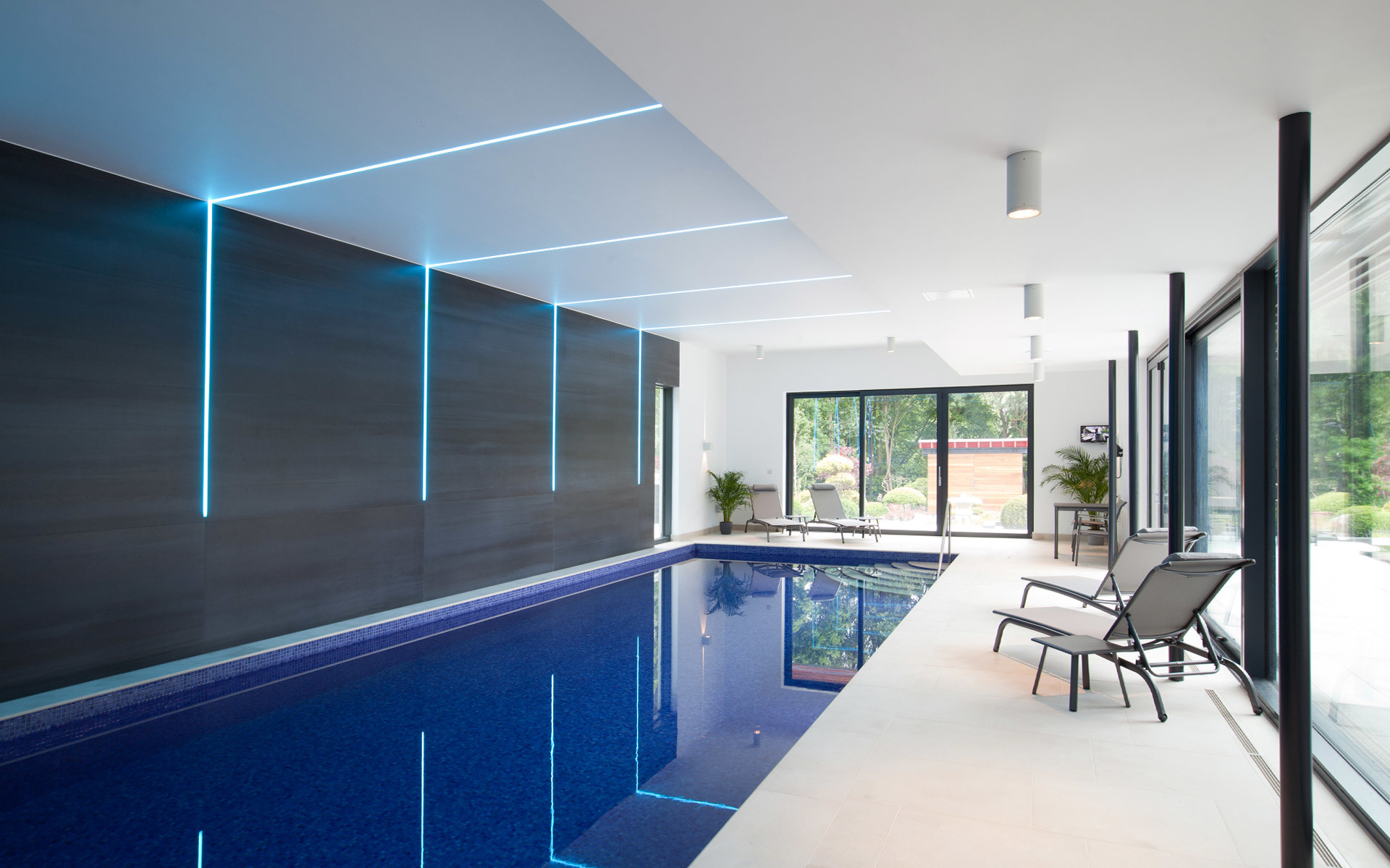 Indoor pool with cyan linear LED lighting on dark wall and ceiling, creating a sleek, modern ambiance with reflections on blue water