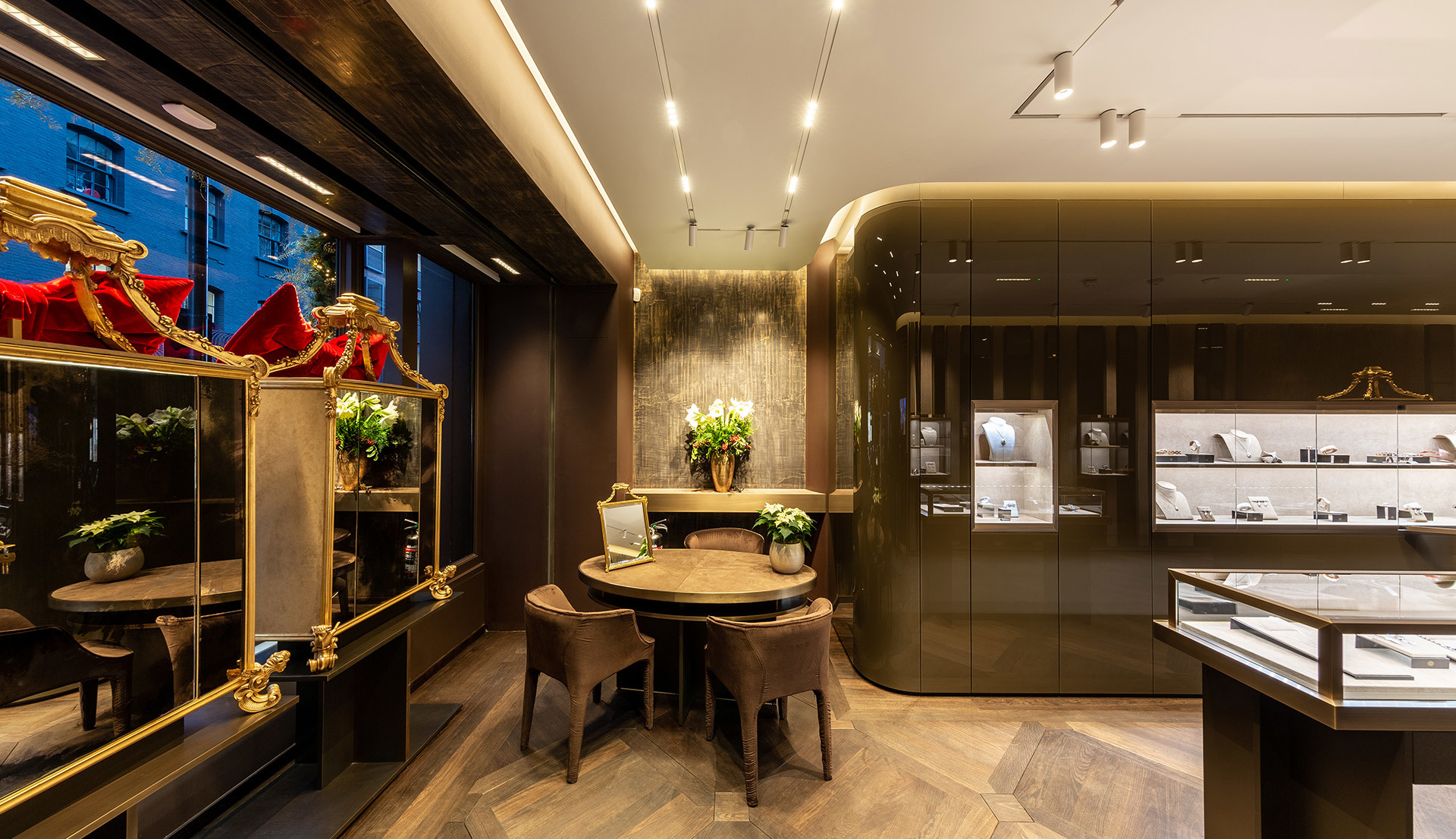 Luxury jewelry boutique interior with recessed ceiling spotlights, display cases, round table, velvet chairs, and herringbone wood floor.
