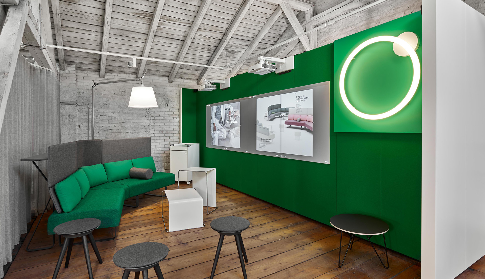 Modern lounge with green sofa, white pendant lamp, and circular LED wall light on a bold green accent wall with exposed wooden beams.
