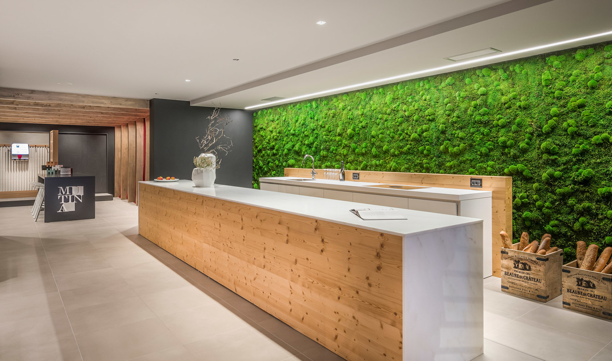 Modern reception with wooden counter, green moss wall, and Artemide linear LED ceiling lights illuminating the space.