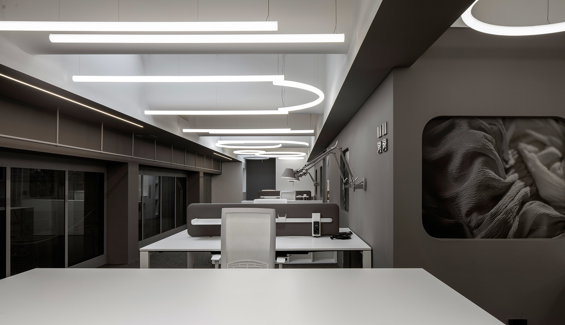 Modern office with Artemide linear and oval pendant lights illuminating workstations in a sleek dark grey interior