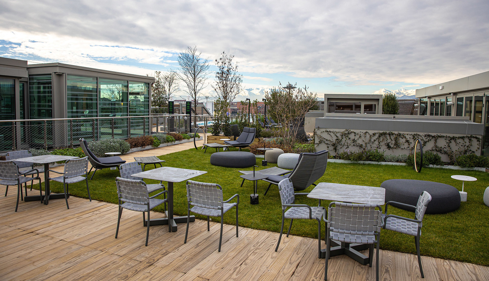 Modern rooftop terrace with outdoor seating, green lawn, grey furniture, and wooden deck under a cloudy sky
