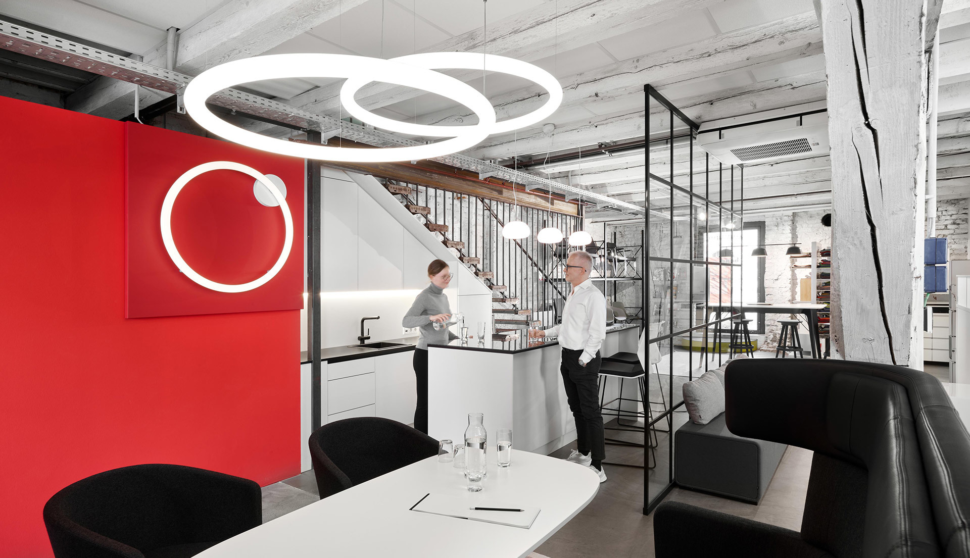 Modern office with Artemide Optical pendant light, interlocking white rings, above a white table; red accent wall and industrial interior.