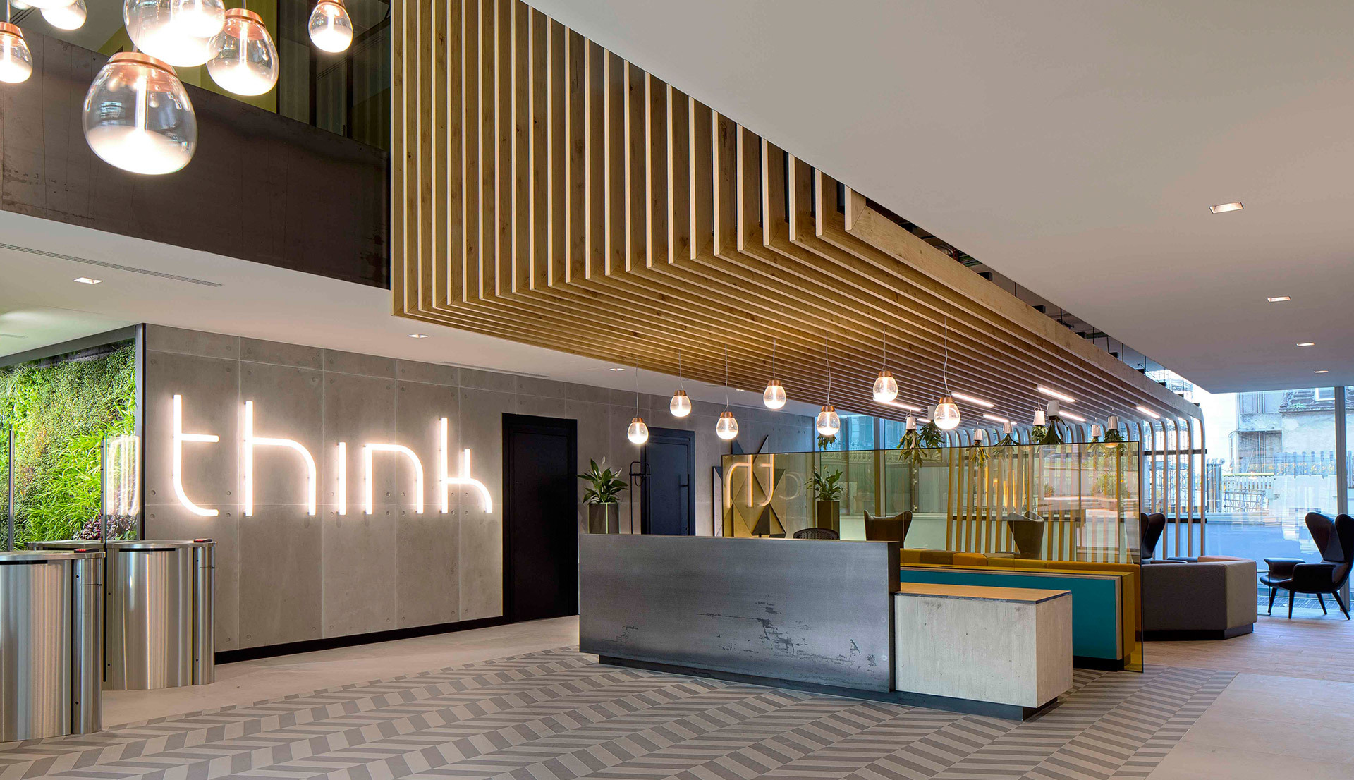 Modern office reception with globe pendant lights, wood slat ceiling, 'think' illuminated sign, and a sleek concrete front desk.
