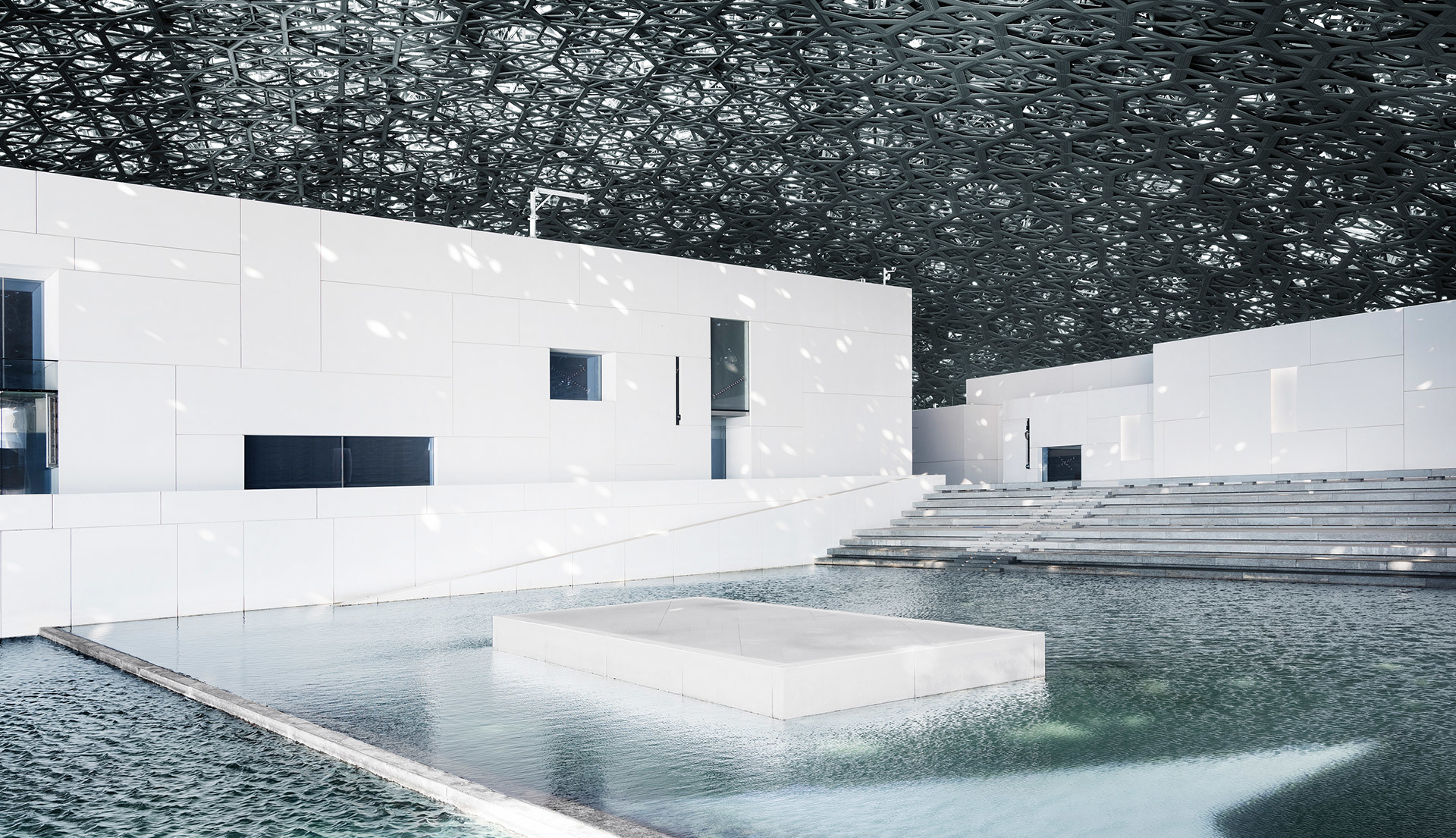 Louvre Abu Dhabi interior courtyard with reflective pool, white walls, and iconic perforated dome casting light patterns