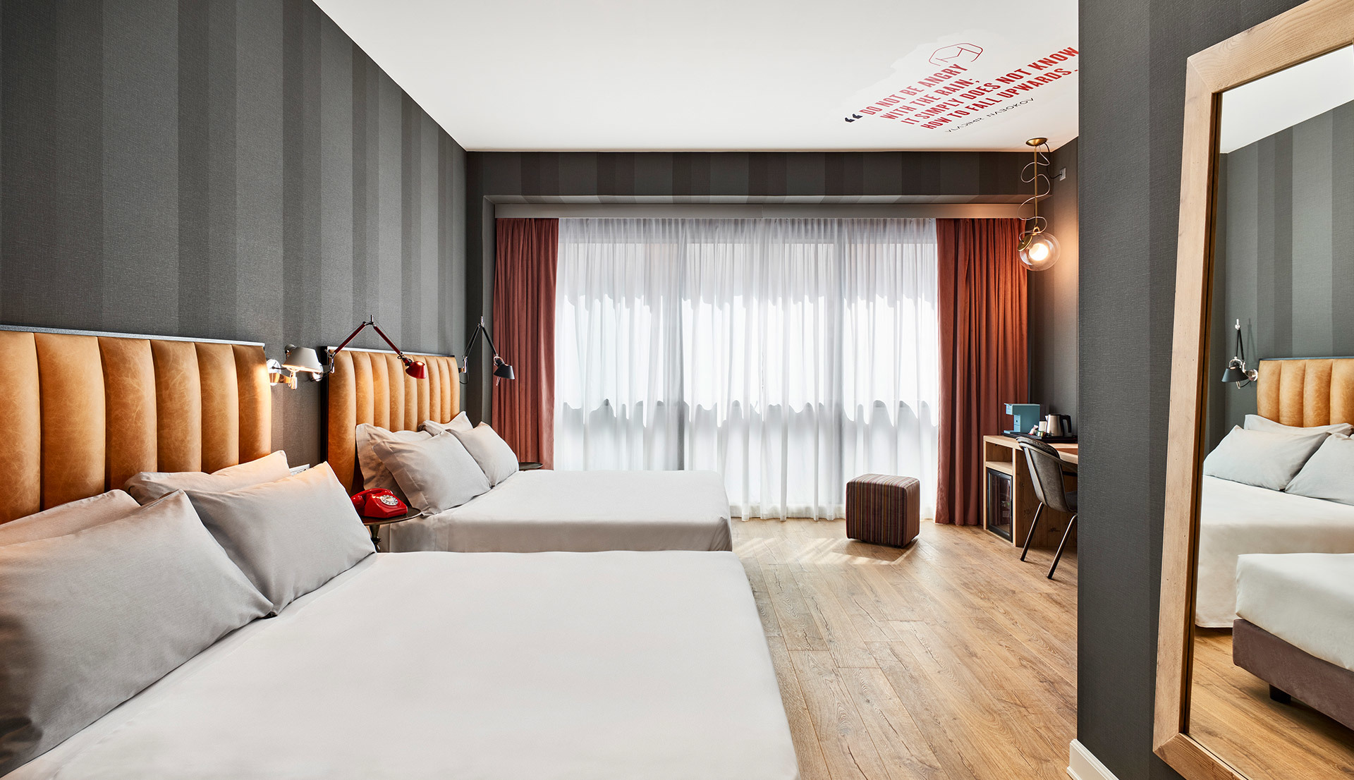 Modern hotel twin bedroom with warm lighting, tan leather headboards, gray striped walls, sheer curtains, and wall-mounted reading lamps.