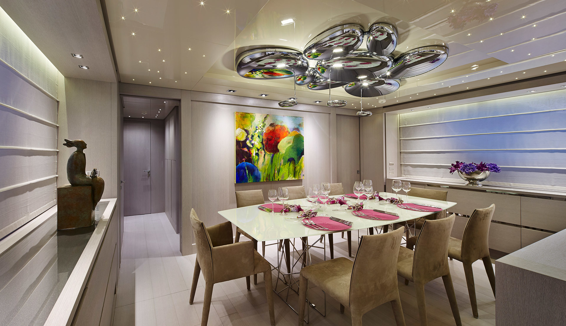 Elegant dining room with a sculptural chrome bubble ceiling pendant lamp above a white table set with pink napkins and crystal glasses.