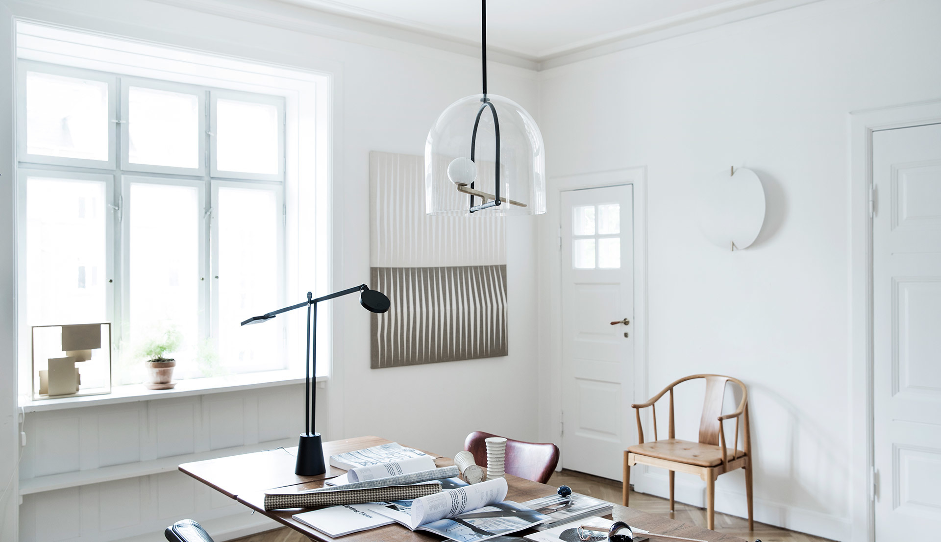 Bright Scandinavian-style room with a glass dome pendant lamp, a black adjustable desk lamp, and a wooden chair.