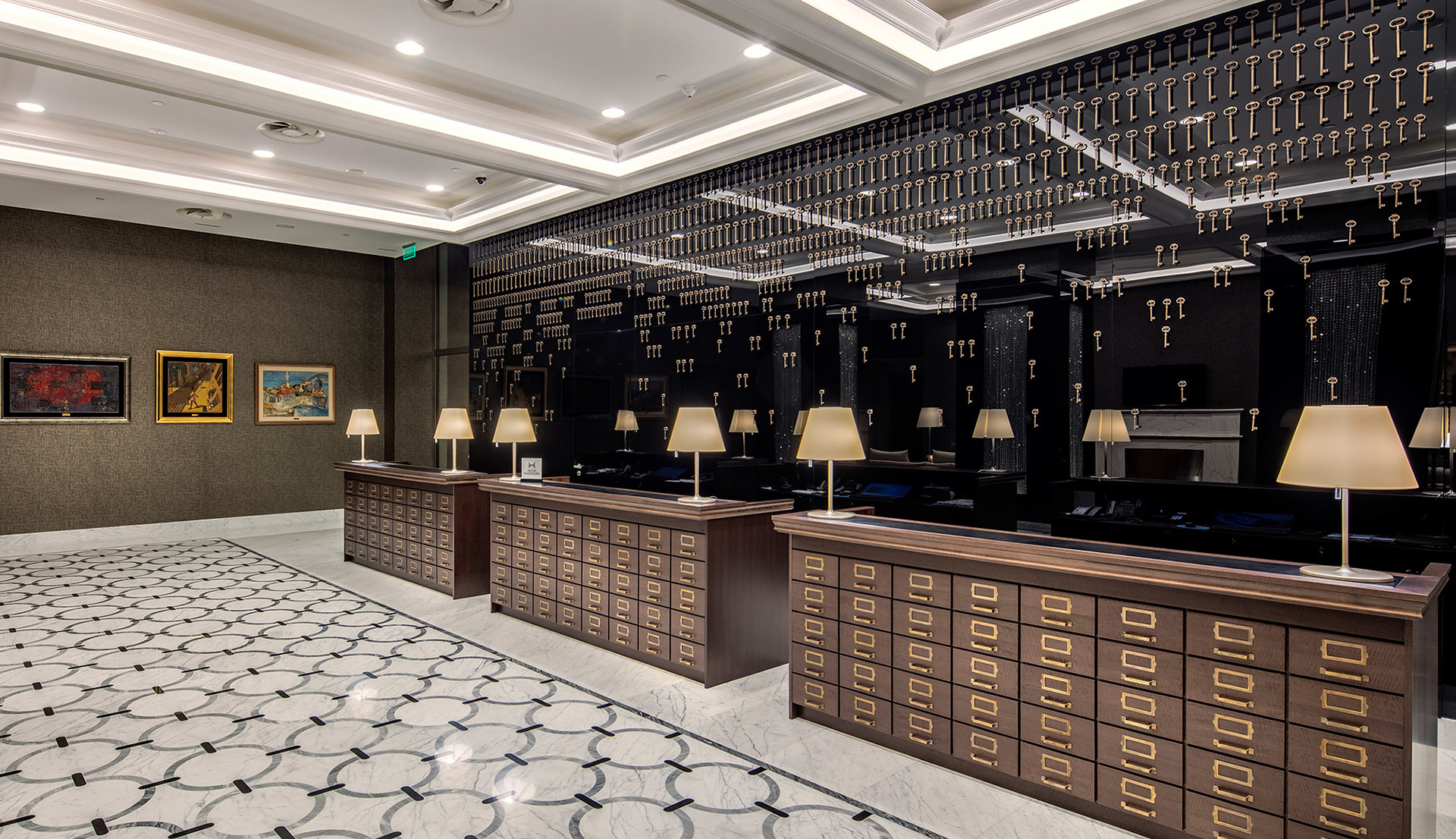 Elegant hotel reception with dark wood counters, table lamps with cream shades, key display wall, and recessed ceiling lighting.