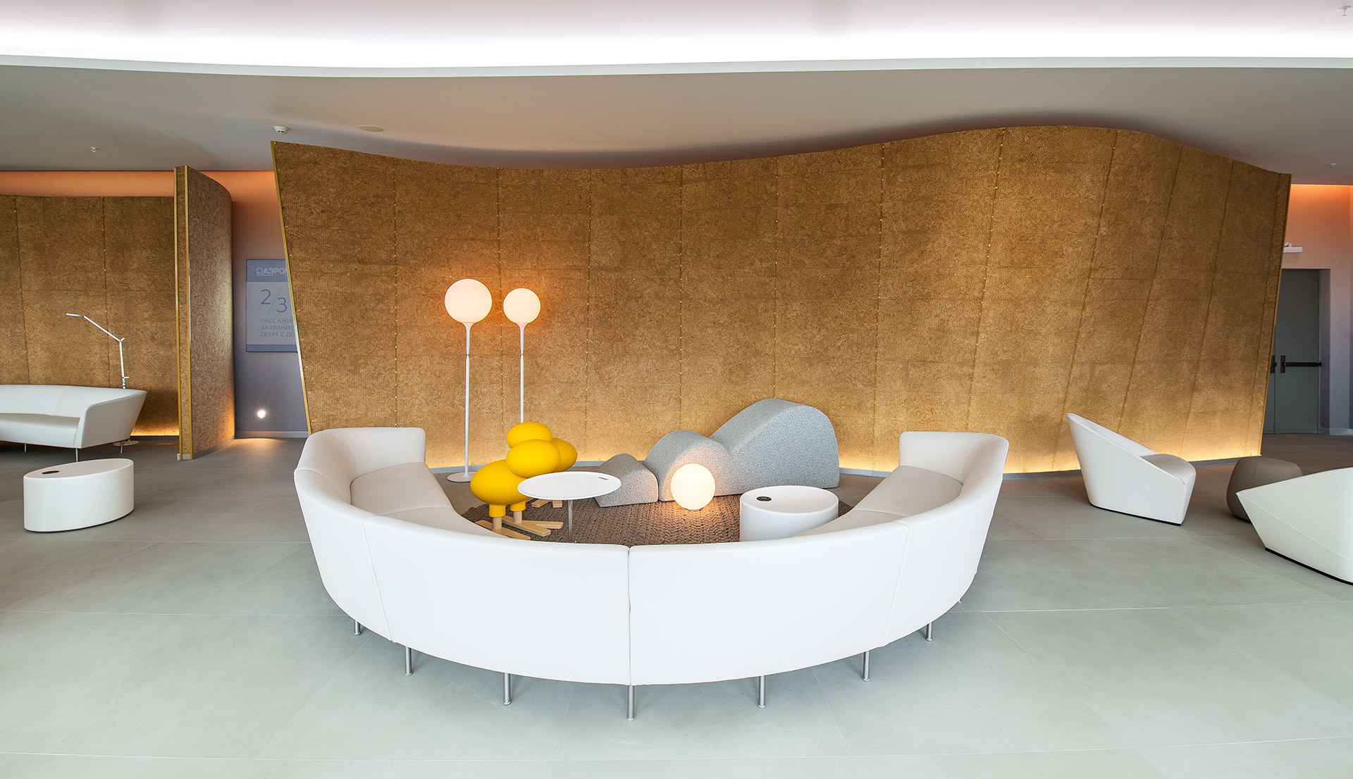 Modern lounge with curved white sofa, yellow floor lamps with spherical shades, and warm-lit cork accent wall in a minimalist interior