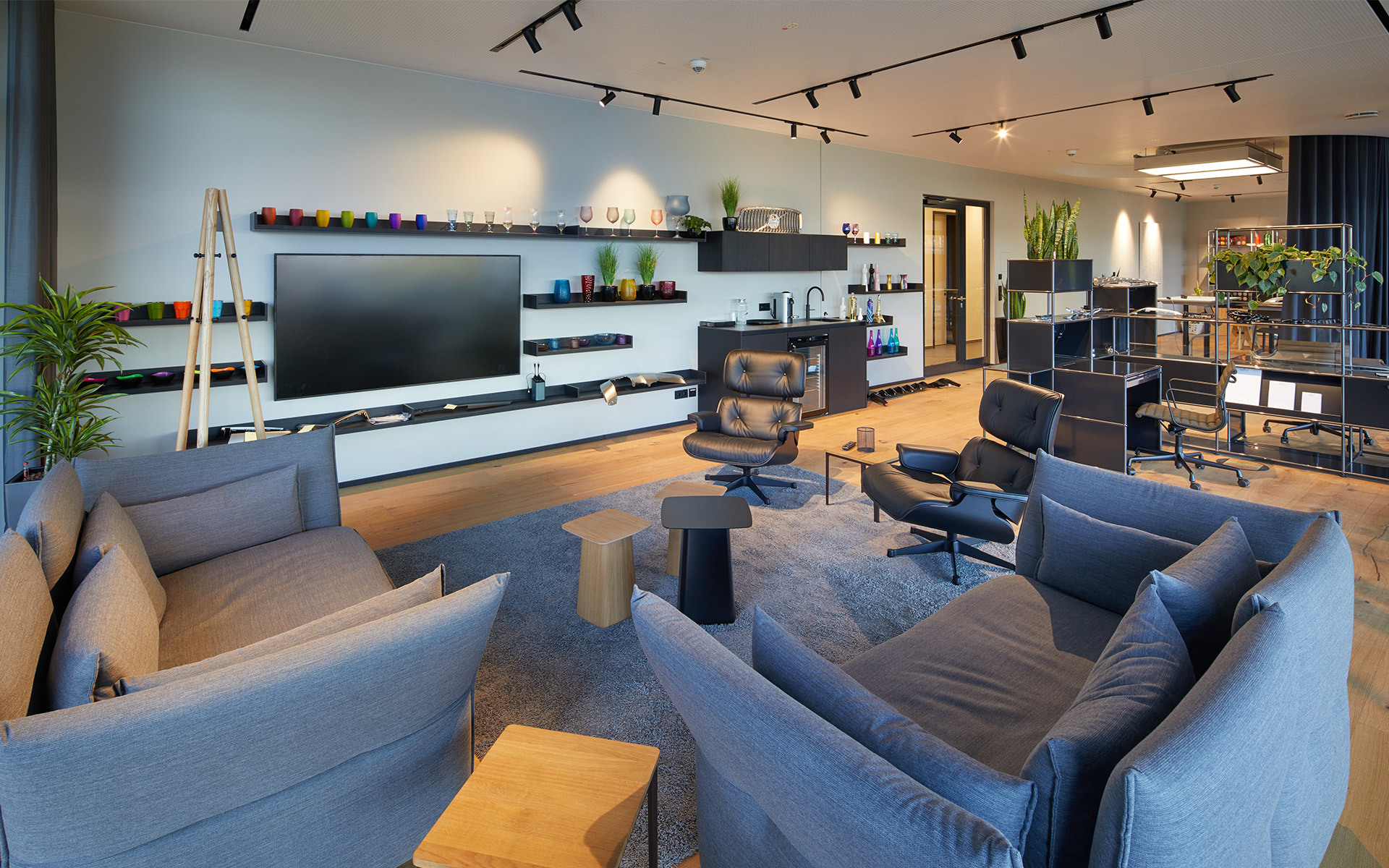 Modern lounge with gray sofas, TV wall unit, and Artemide track lighting on ceiling illuminating a stylish open-plan living space