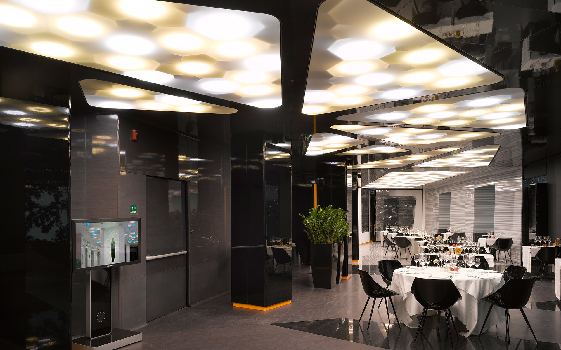 Modern restaurant interior with dark ceiling featuring organic-shaped recessed luminaires arranged in clusters, illuminating dining tables.