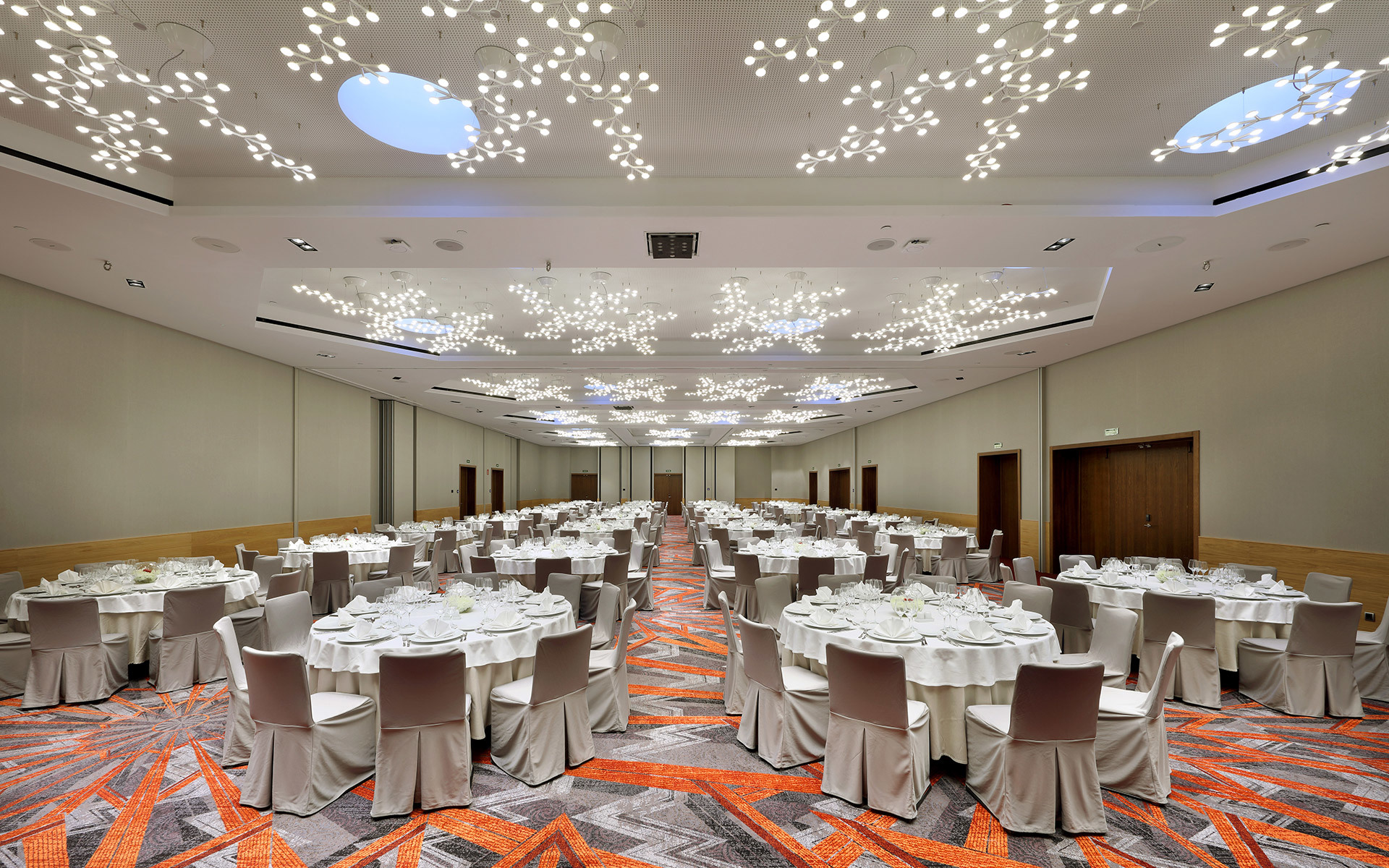Elegant ballroom with round banquet tables set for dining, illuminated by branching Artemide pendant lights creating a starry ceiling effect.