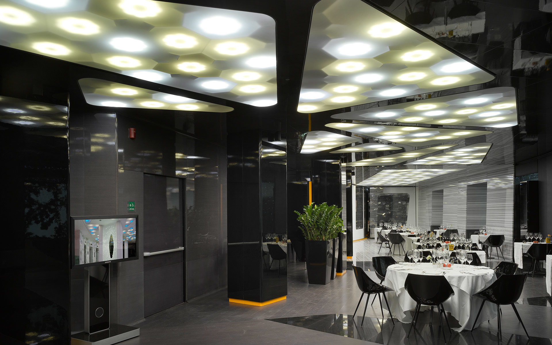 Modern restaurant interior with dark décor featuring Artemide ceiling lights with circular LED panels arranged in geometric patterns.
