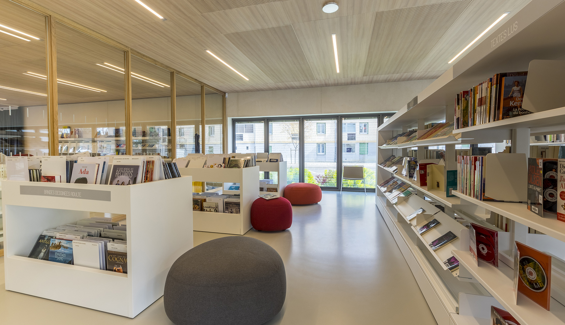 Modern library interior with Artemide recessed linear ceiling lights illuminating white shelves, books, and colorful seating poufs.